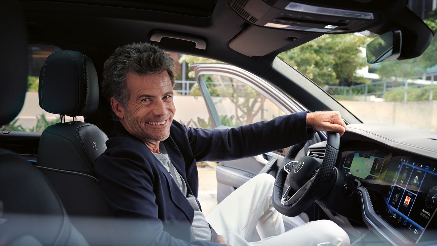 Ein Mann auf dem Vordersitz eines parkenden VW Touareg R-Line blickt lächelnd in die Kamera.
