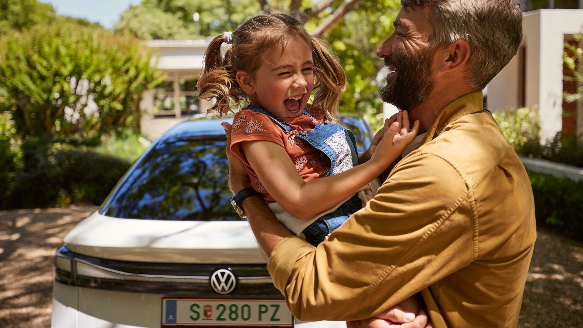 Ein Vater hält Kind im Arm, beide lachen, man sieht das Heck des VW ID.7