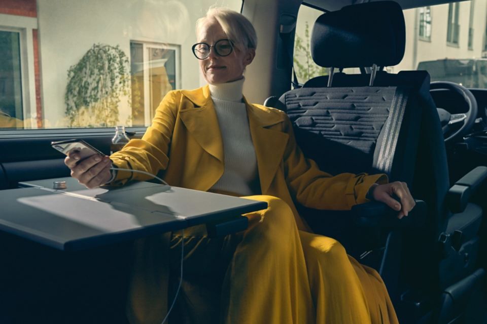 Eine Frau sitzt im VW Multivan 6.1. Ihre Hand hält ein Smartphone und lehnt am Beistelltisch.