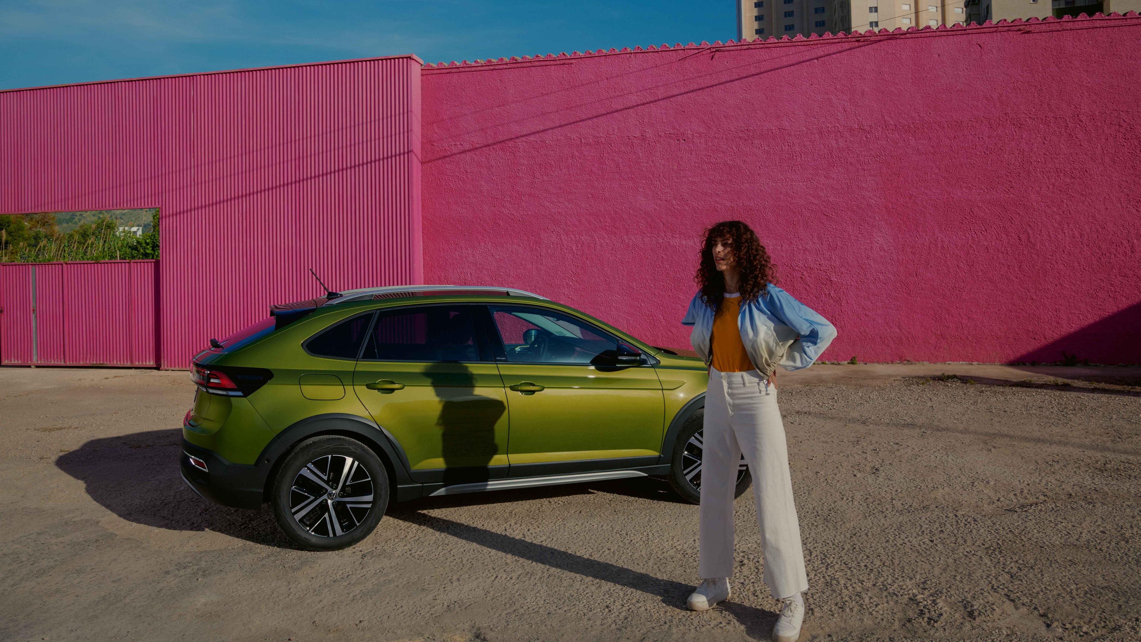 VW Taigo in Grün auf Parkplatz, Seite sichtbar, Frau steht vor Auto