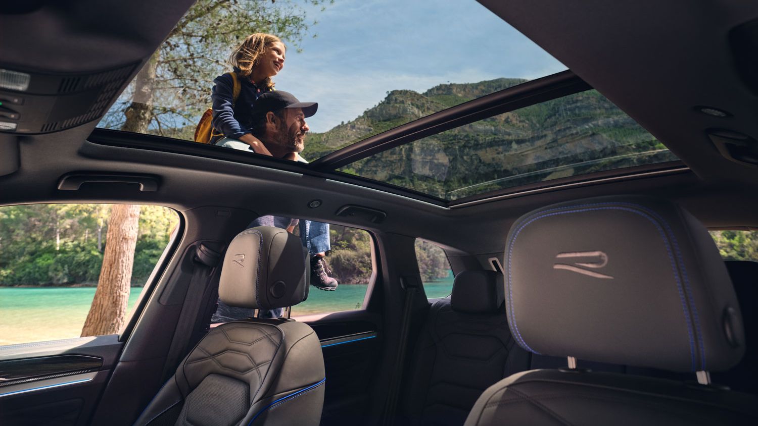 Blick durch das Panoramadach eines VW Touareg R eHybrid, ein Mann trägt ein Mädchen auf seien Schultern
