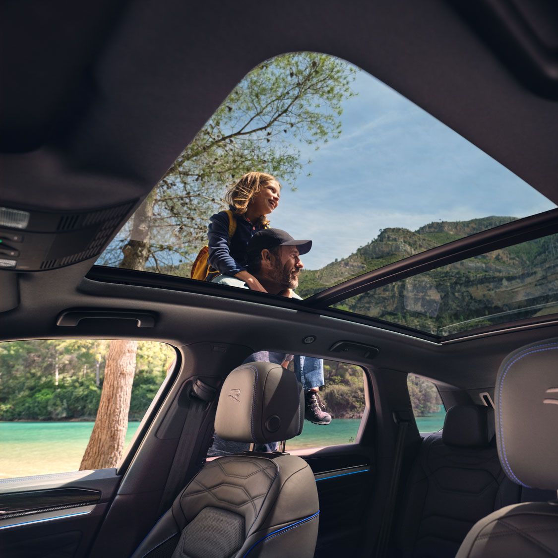 Blick durch das Panoramadach eines VW Touareg R eHybrid, ein Mann trägt ein Mädchen auf seien Schultern