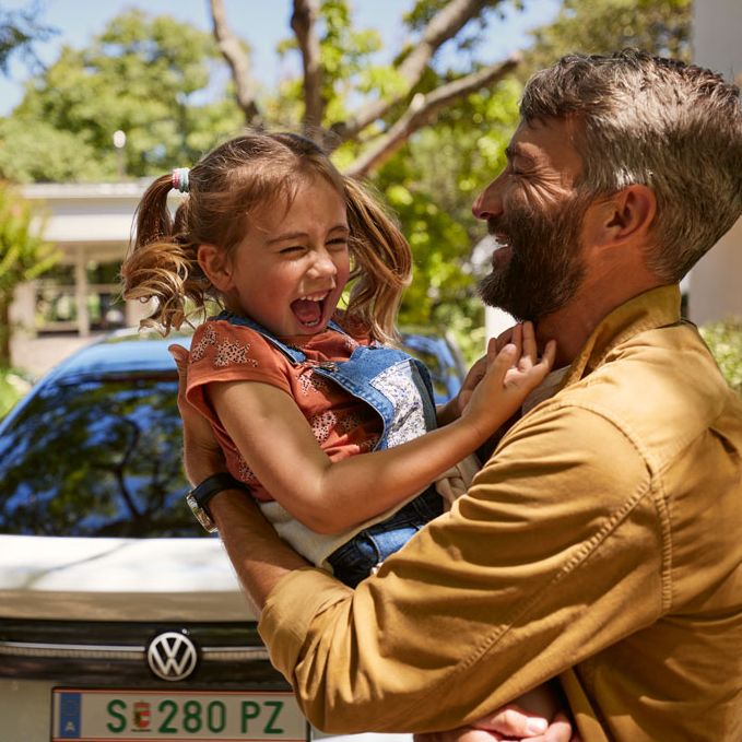 Ein Vater hält seine lachende Tochter, im Hintergrund ist ein VW ID.7 zu sehen