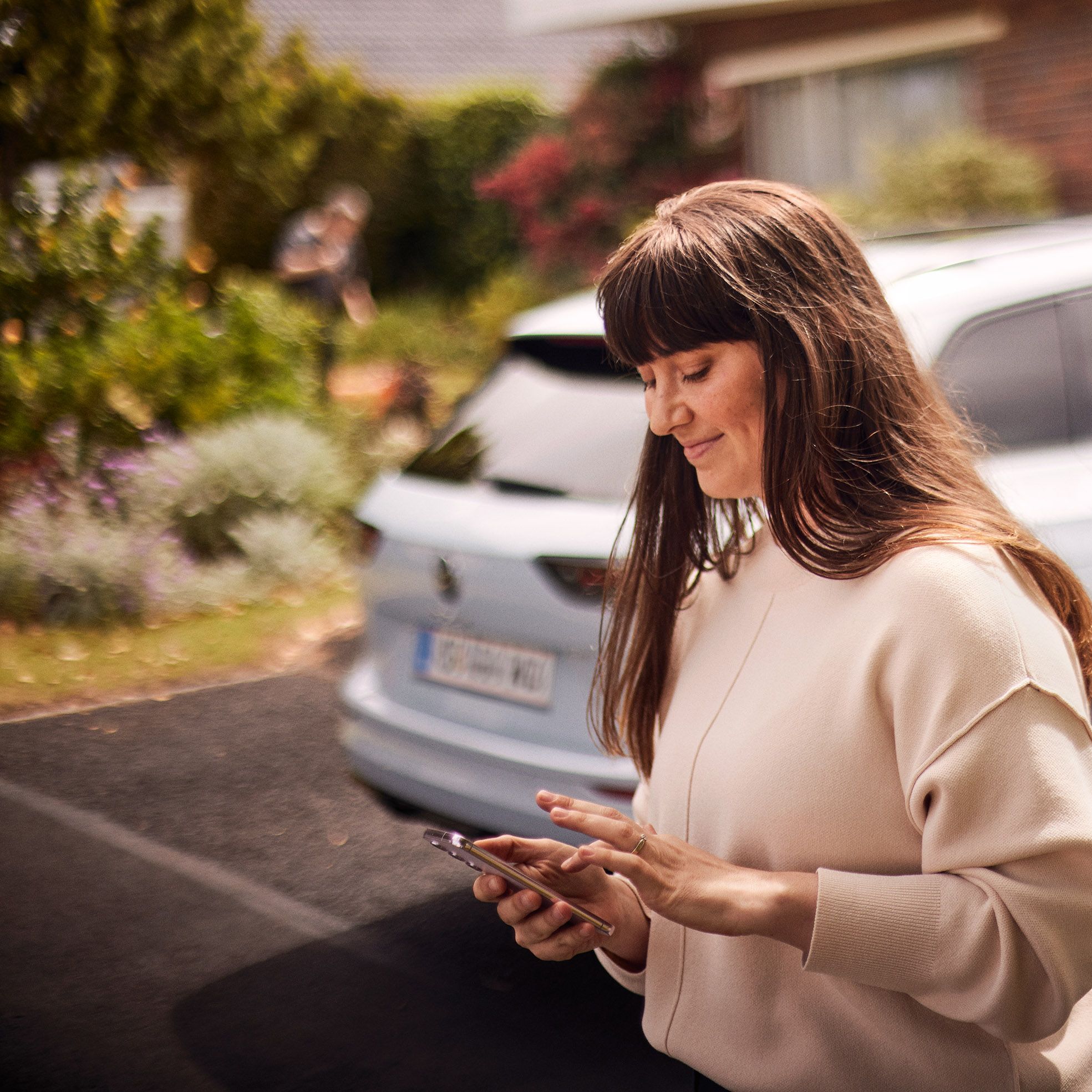 Frau steht vor VW Golf Variant und nutzt die Volkswagen App auf ihrem Smartphone