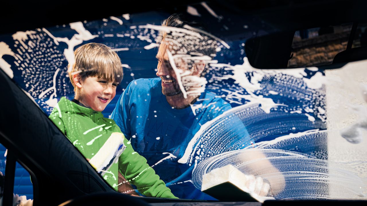 Ein Vater mit Sohn wäscht die Windschutzscheibe eines Volkswagen
