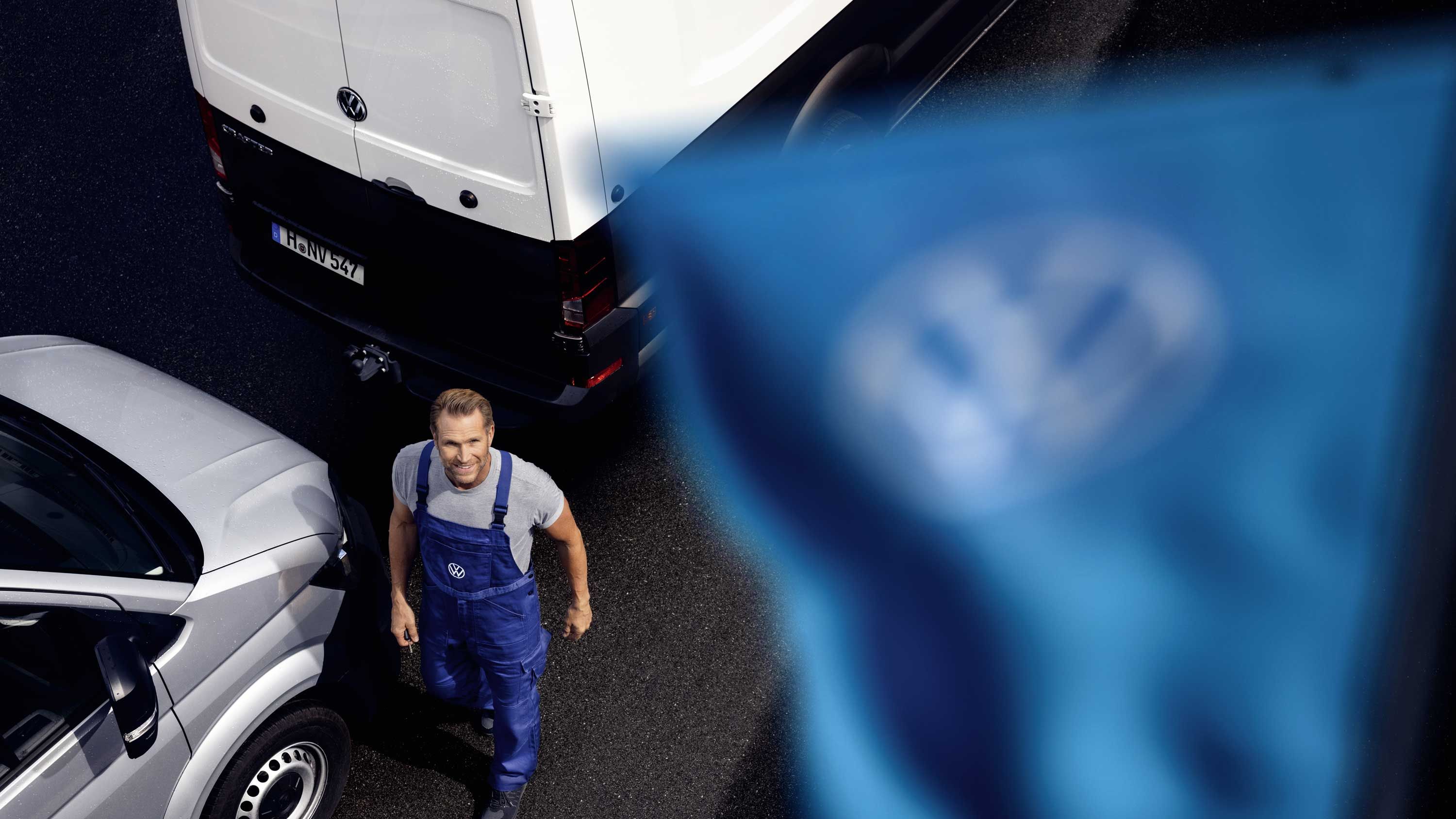 VW Service Mitarbeiter steht neben Volkswagen Nutzfahrzeugen