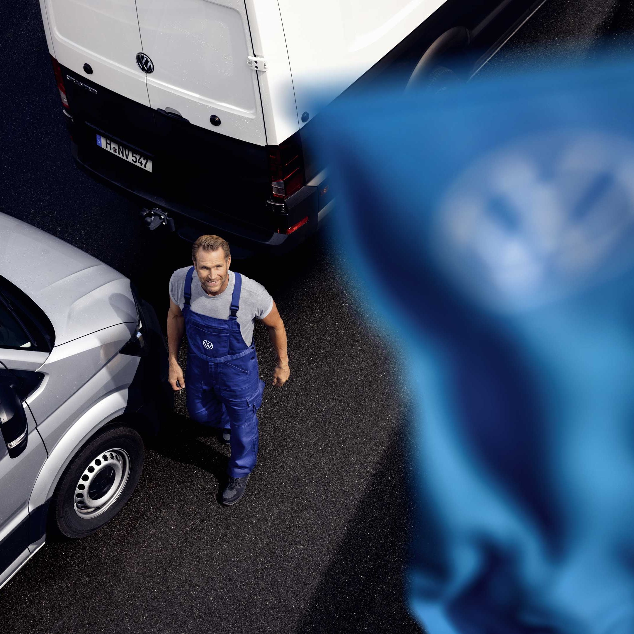 VW Service Mitarbeiter steht neben Volkswagen Nutzfahrzeugen