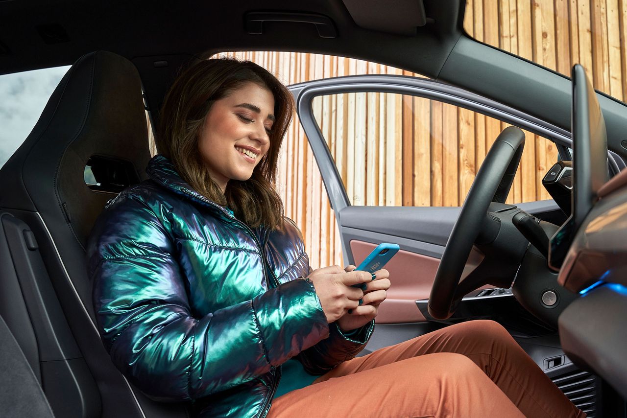 Eine junge Frau sitzt in einem Volkswagen und blickt auf ihr Smartphone