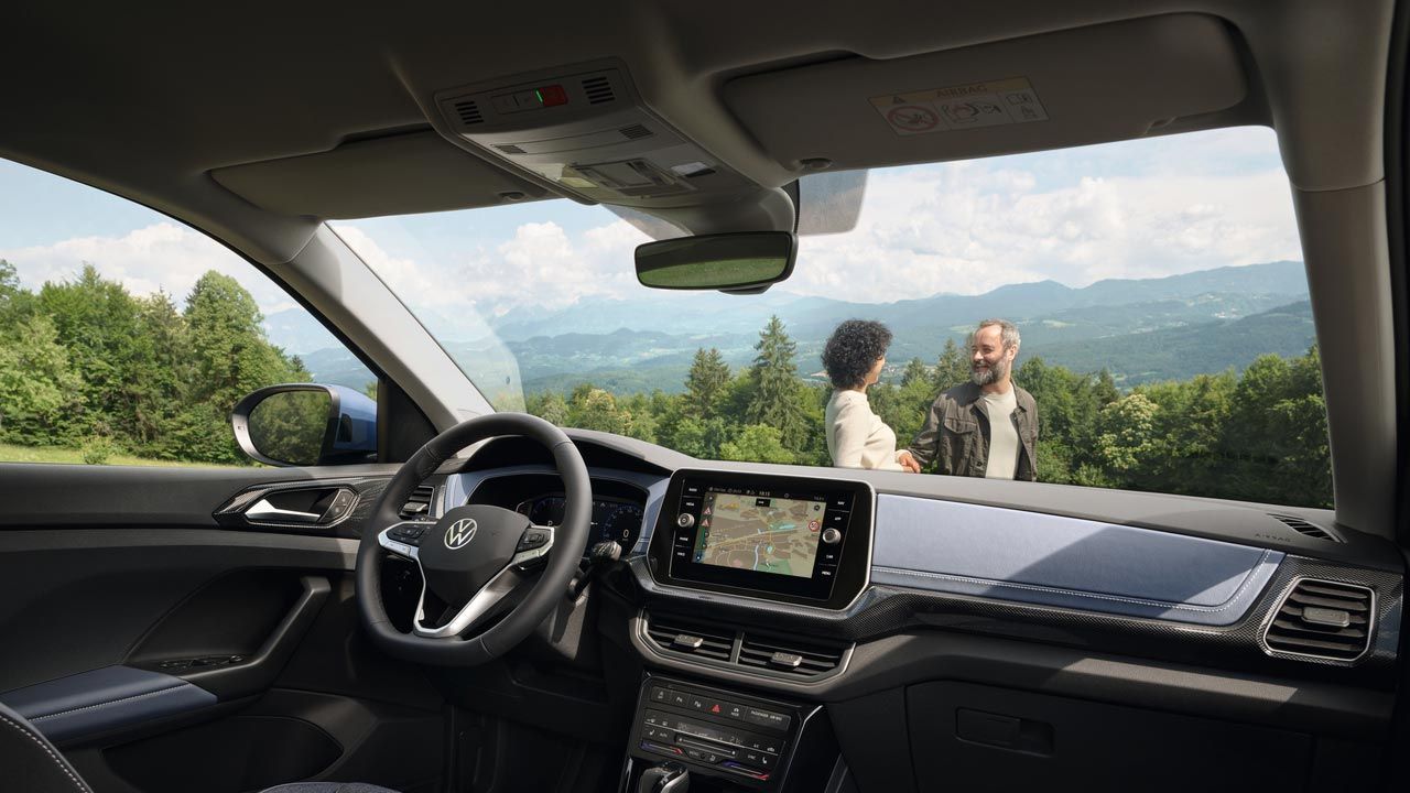 Aussicht vom Beifahrersitz aus auf einen Mann und eine Frau vor hügeliger Wald-Landschaft.