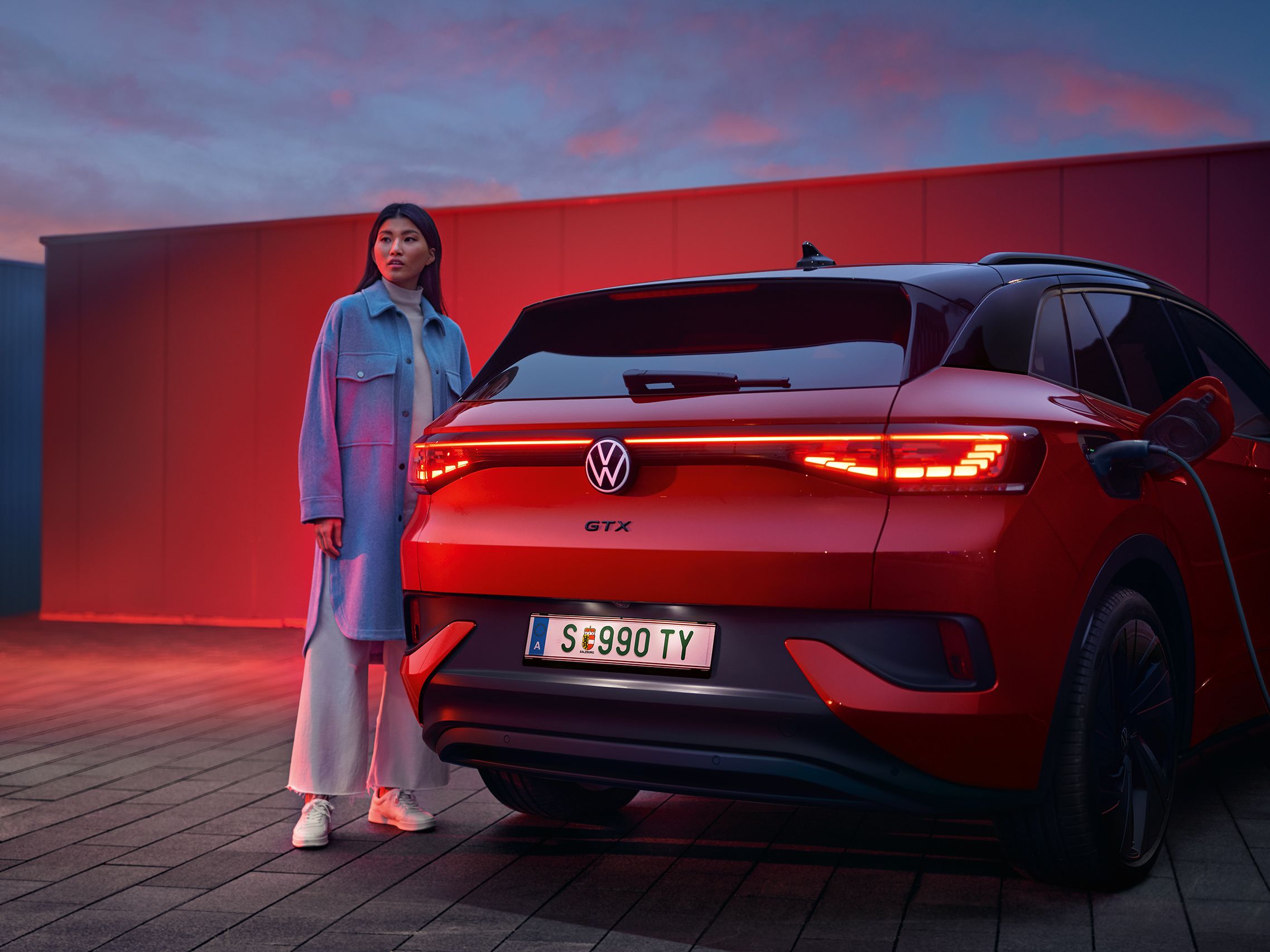 Heckansicht des VW ID.4 GTX 4MOTION, eine Frau steht daneben