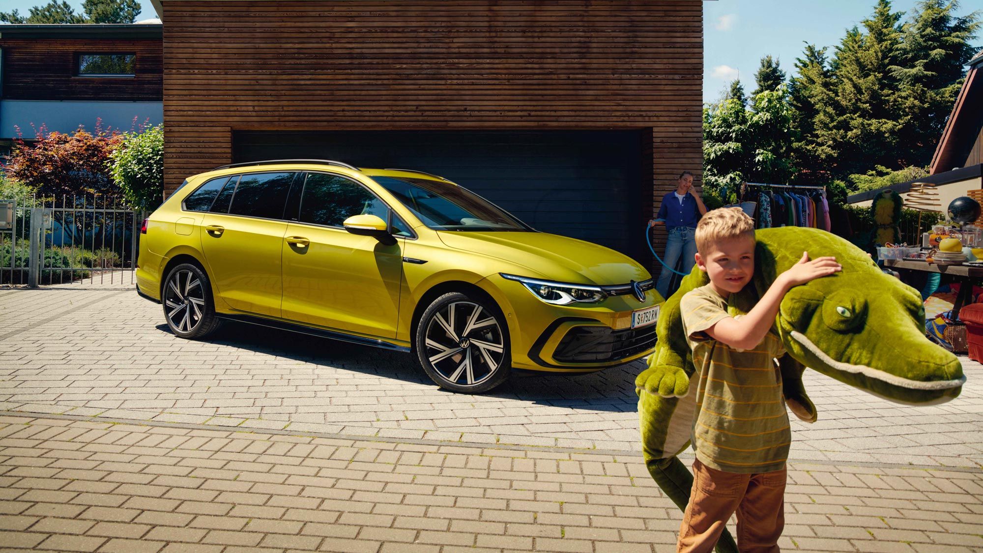 Junge mit Stoff-Krokodil steht vor gelbem VW Golf Variant