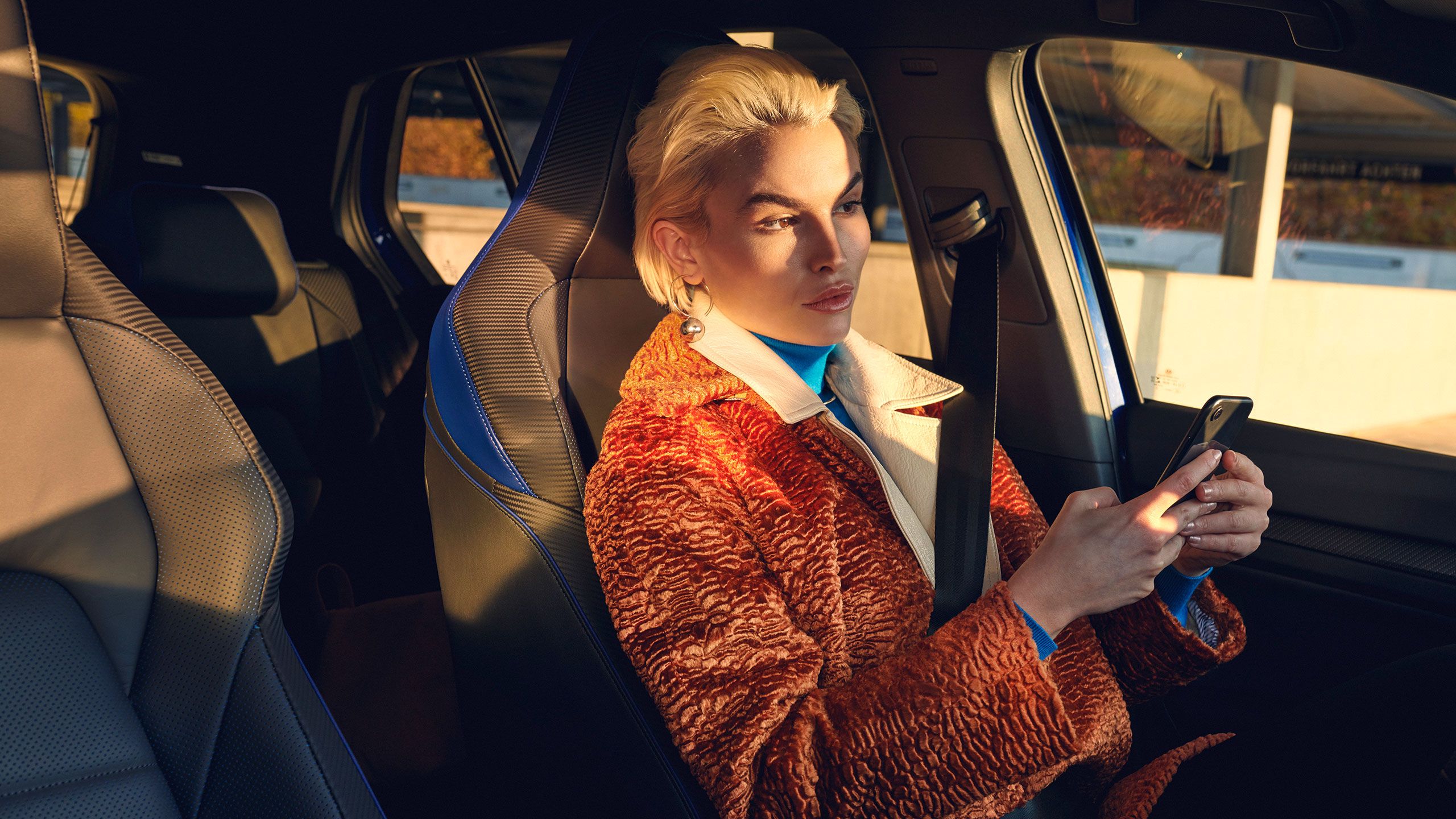 Eine Frau wartet mit ihrem Smartphone in der Hand in ihrem VW R-Modell