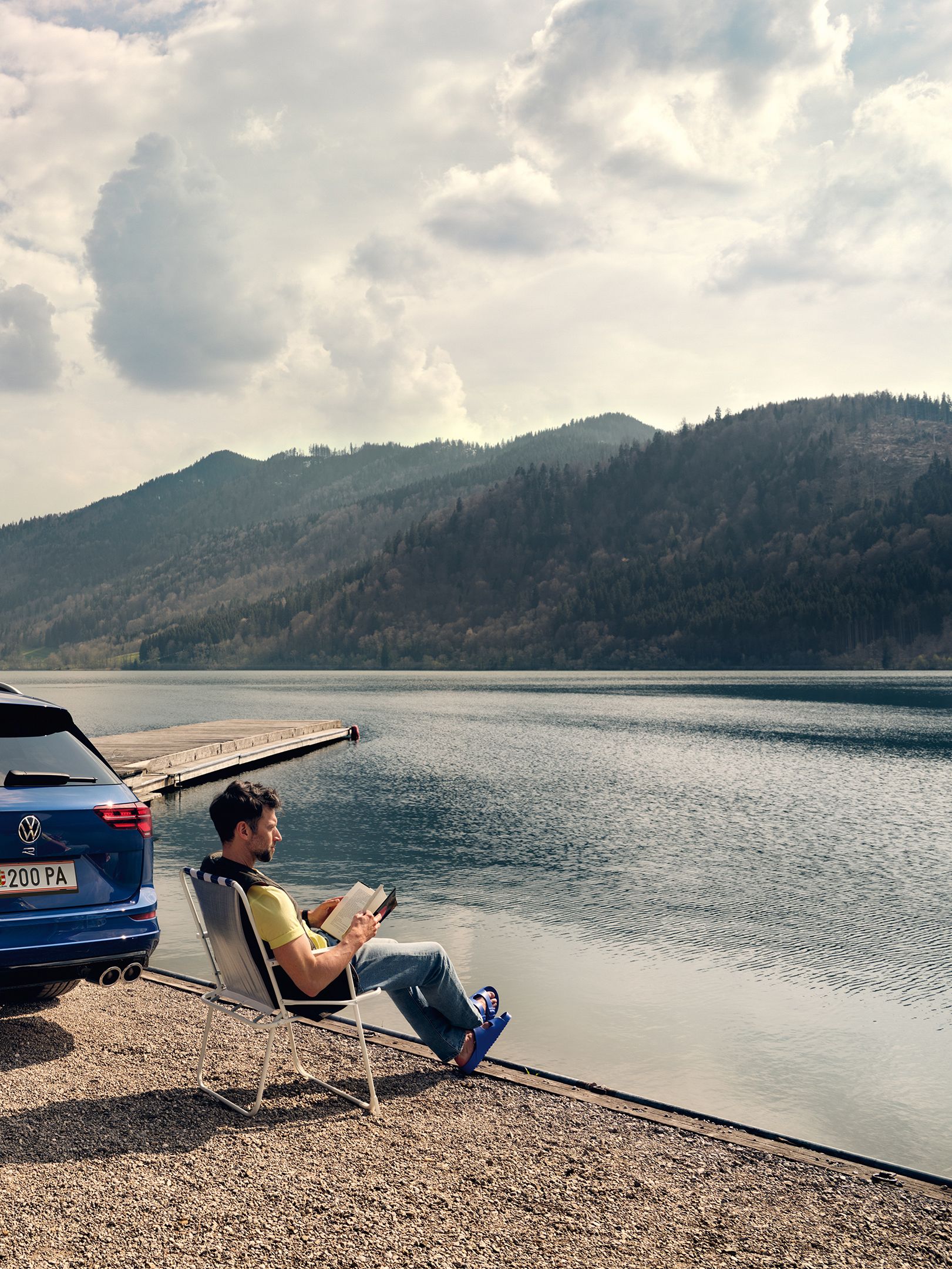 VW Golf R Variant steht an einem See, daneben sitzt ein Mann in einem Campingstuhl