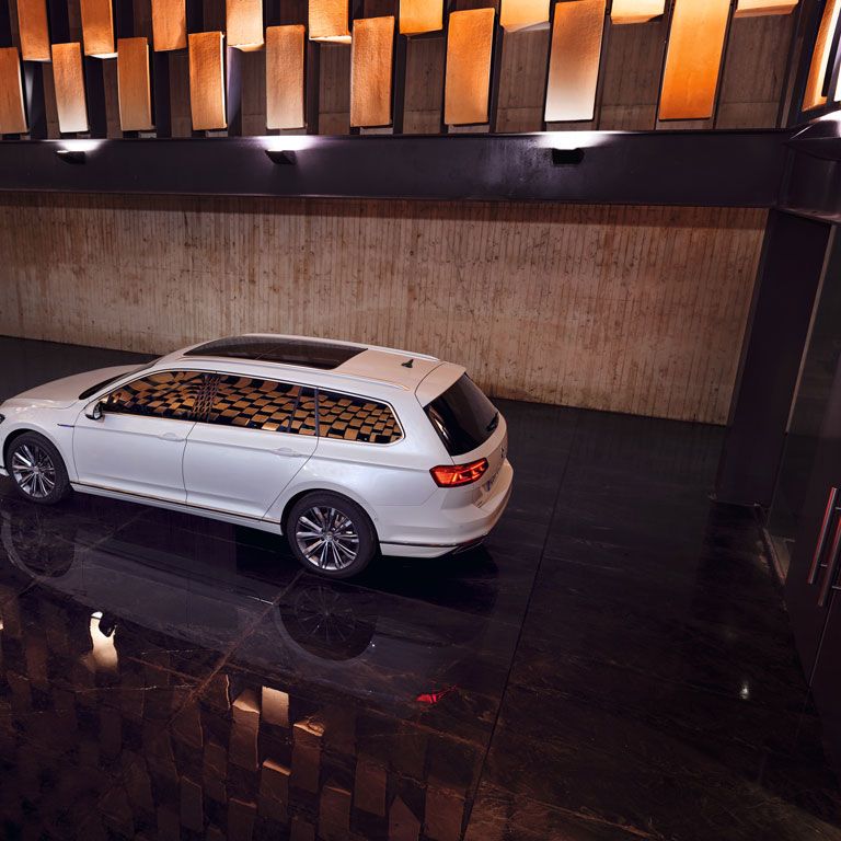 Ein weißer VW Passat steht in einer Halle mit dunklem Boden und wird von der Decke angestrahlt.