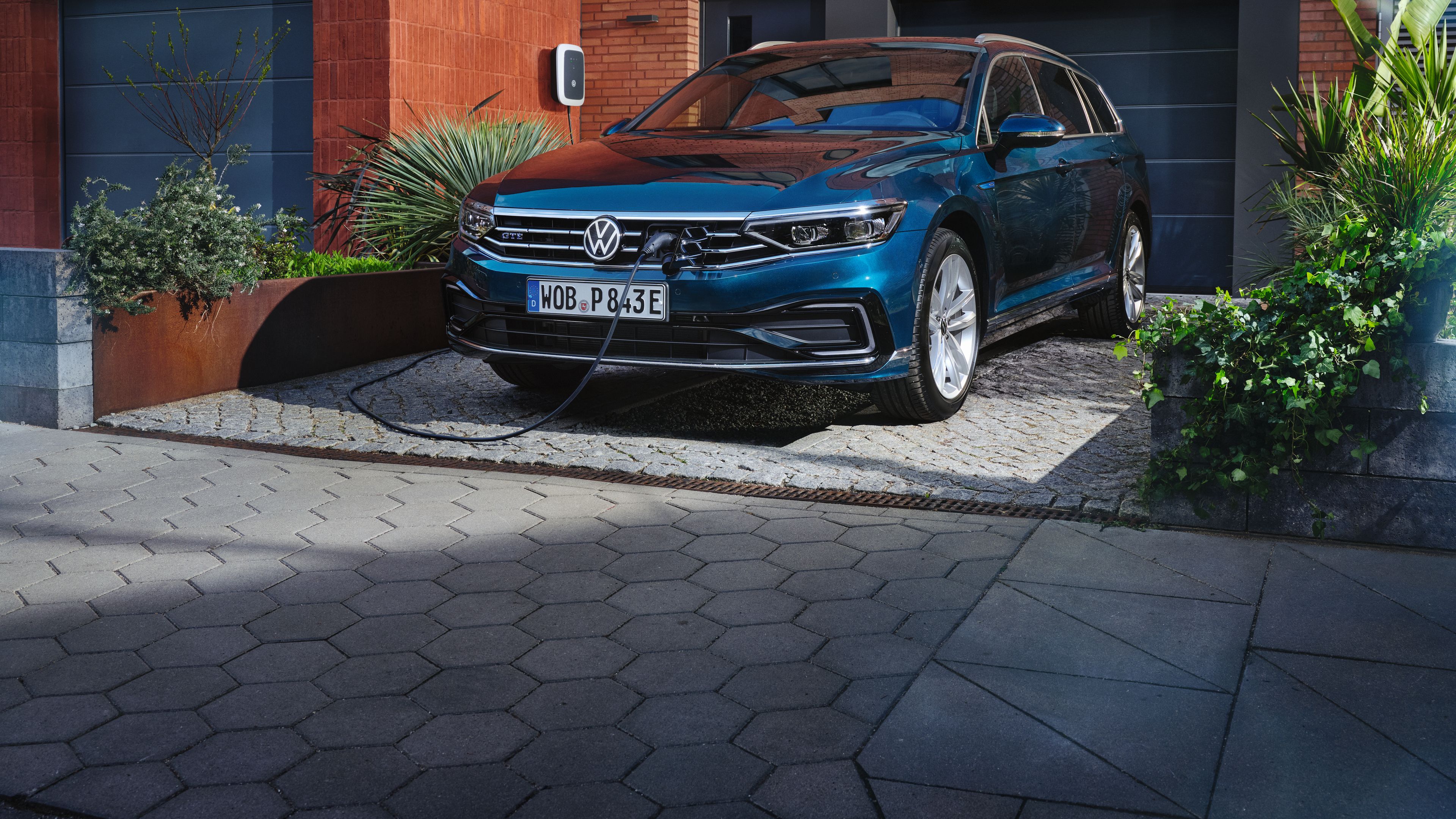 VW Passat Variant GTE steht ladend auf einem Parkplatz vor einem Haus. 