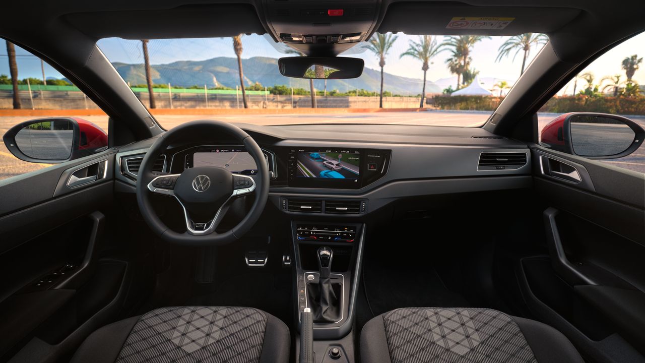 Interieur des VW Taigo mit Digital Cockpit Pro und Infotainmentsystem, Blick durch die Windschutzscheibe auf einen Parkplatz mit Palmen 