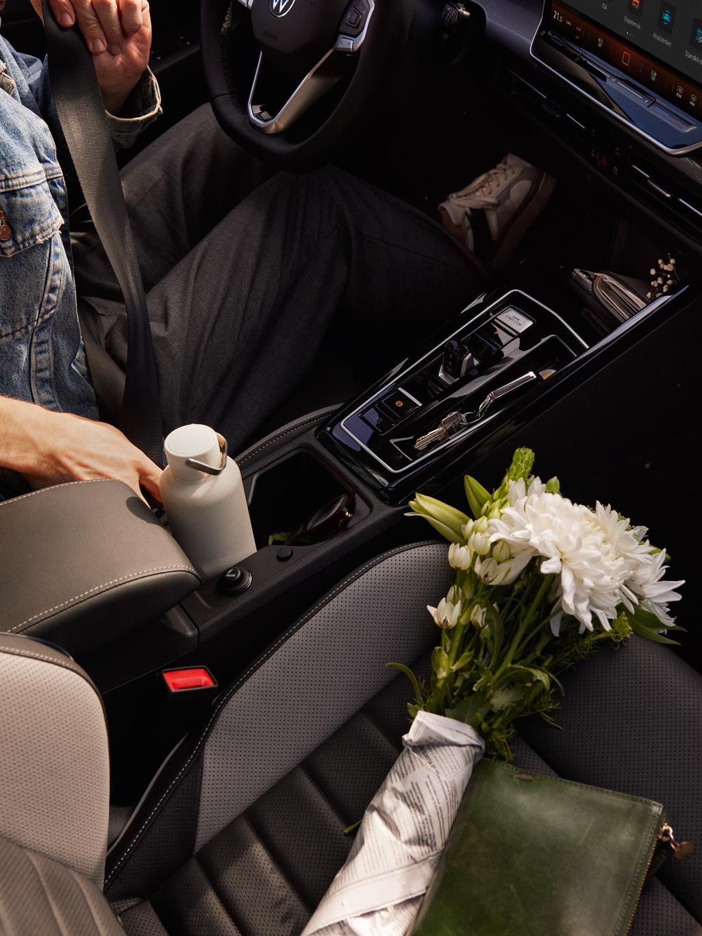 Ein Mann sitzt auf dem Fahrersitz eines VW Golf und schnallt sich an, auf dem Beifahrersitz liegen Blumen