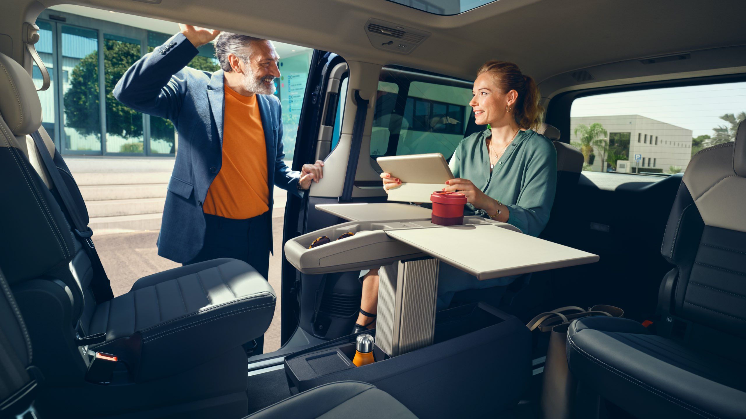 Eine Frau sitzt mit ihrem Tablet am Multifunktionstisch im neuen VW Multivan T7 2021.