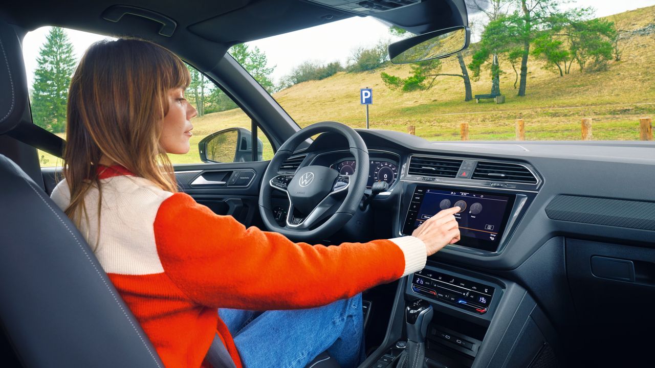 Eine Frau sitzt auf dem Fahrersitz des VW Tiguan Allspace und bedienet das Infotainment-System