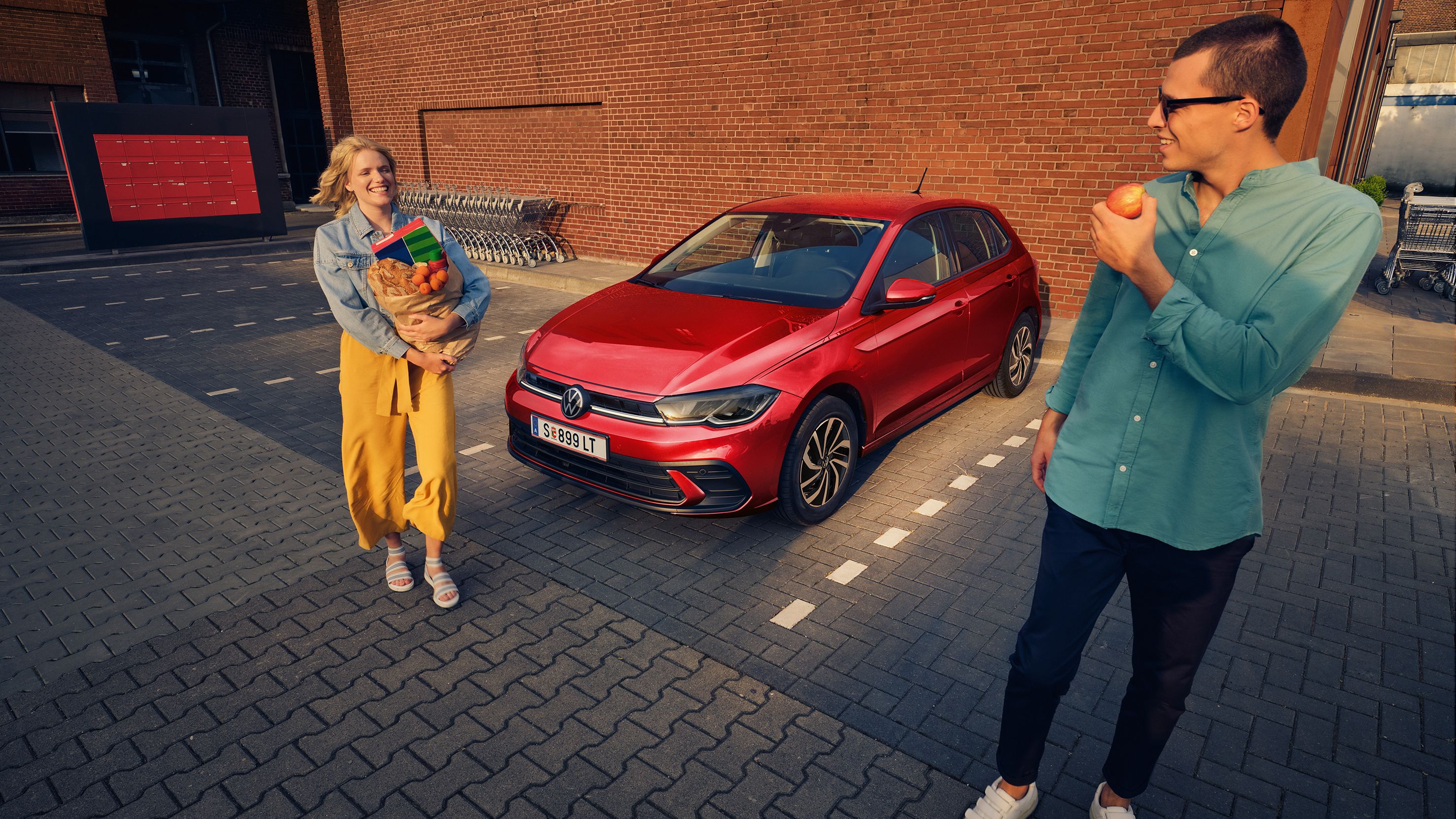 Frau und Mann gehen vor einem geparkten roten VW Polo Life