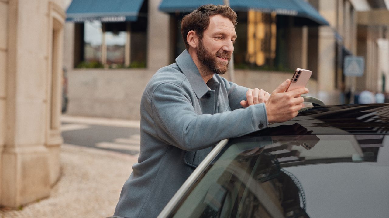 Mann lehnt an einem Volkswagen und schaut auf sein Mobiltelefon