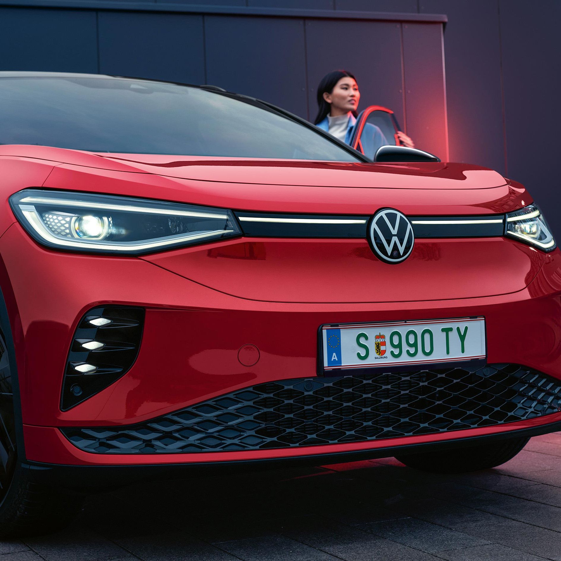 VW ID.4 GTX in Rot mit geöffneter Fahrertür. Frau steht an der Tür und guckt nach vorne.