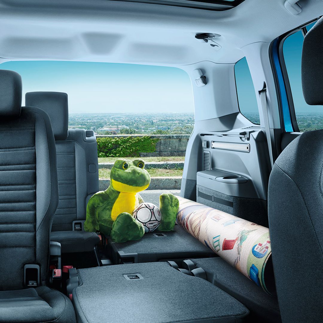 Umgeklappte Rücksitzbänke des VW Touran, ein eingerollter Teppich und ein Froschkuscheltier liegen auf der freien Fläche. 