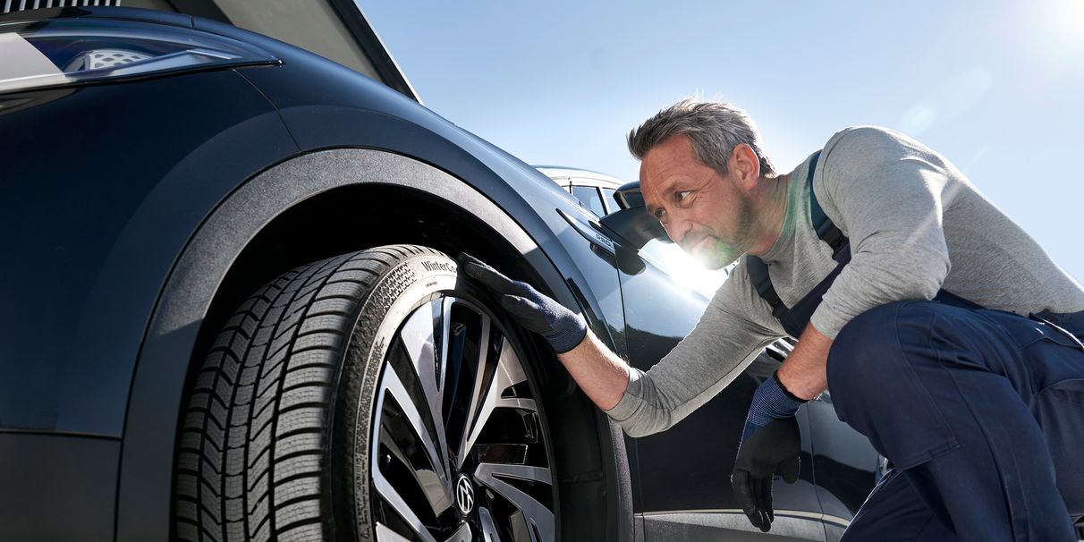 Mechaniker beim Prüfen der Reifen eines VW Fahrzeuges