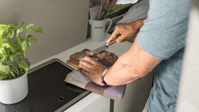 Mann schneidet Brot in der geräumigen Küche des VW Grand California.