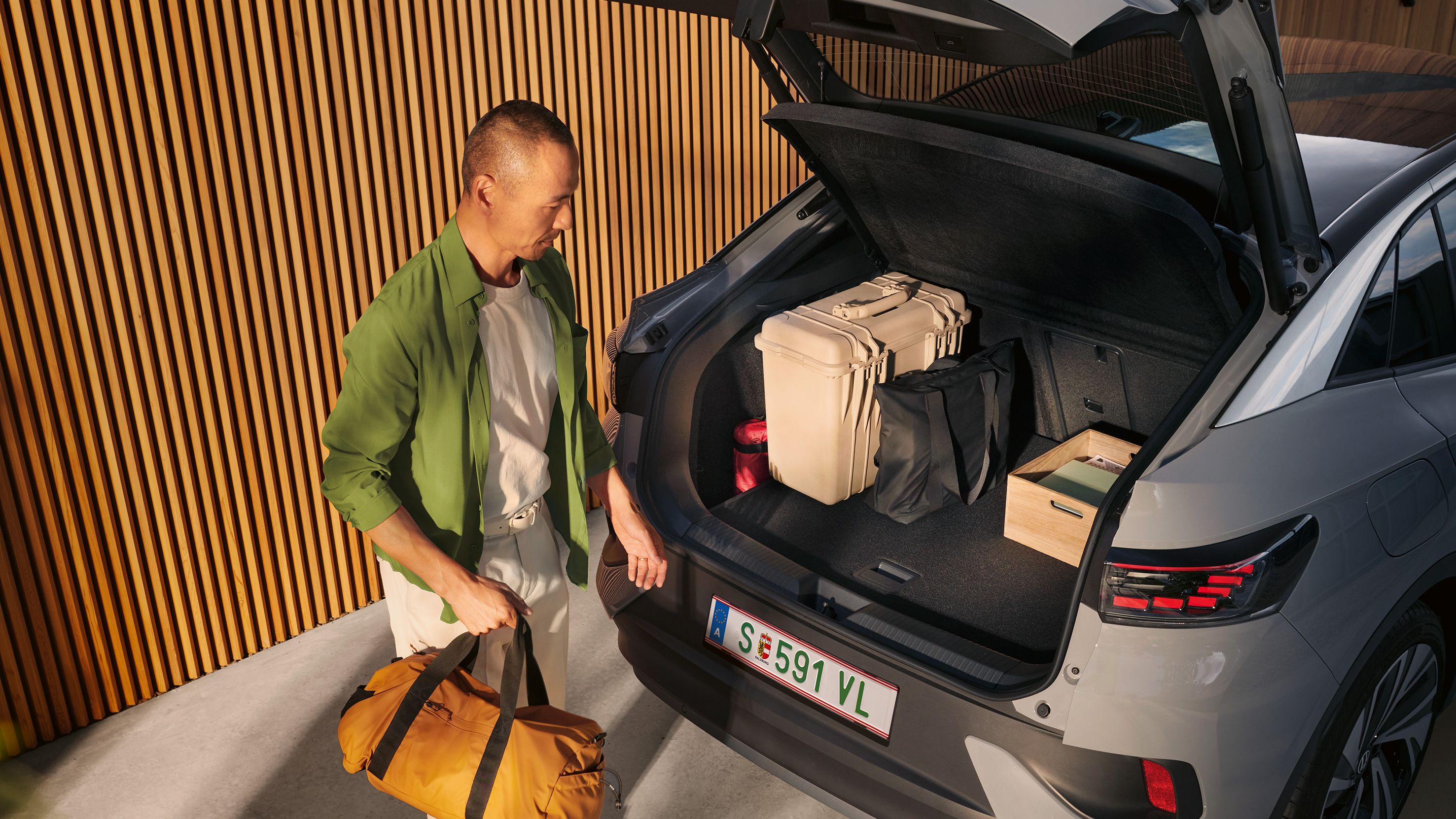 VW ID.5 mit geöffnetem Kofferraum und Gepäck darin, unter der offenen Heckklappe steht ein Mann mit einer Tasche in der Hand