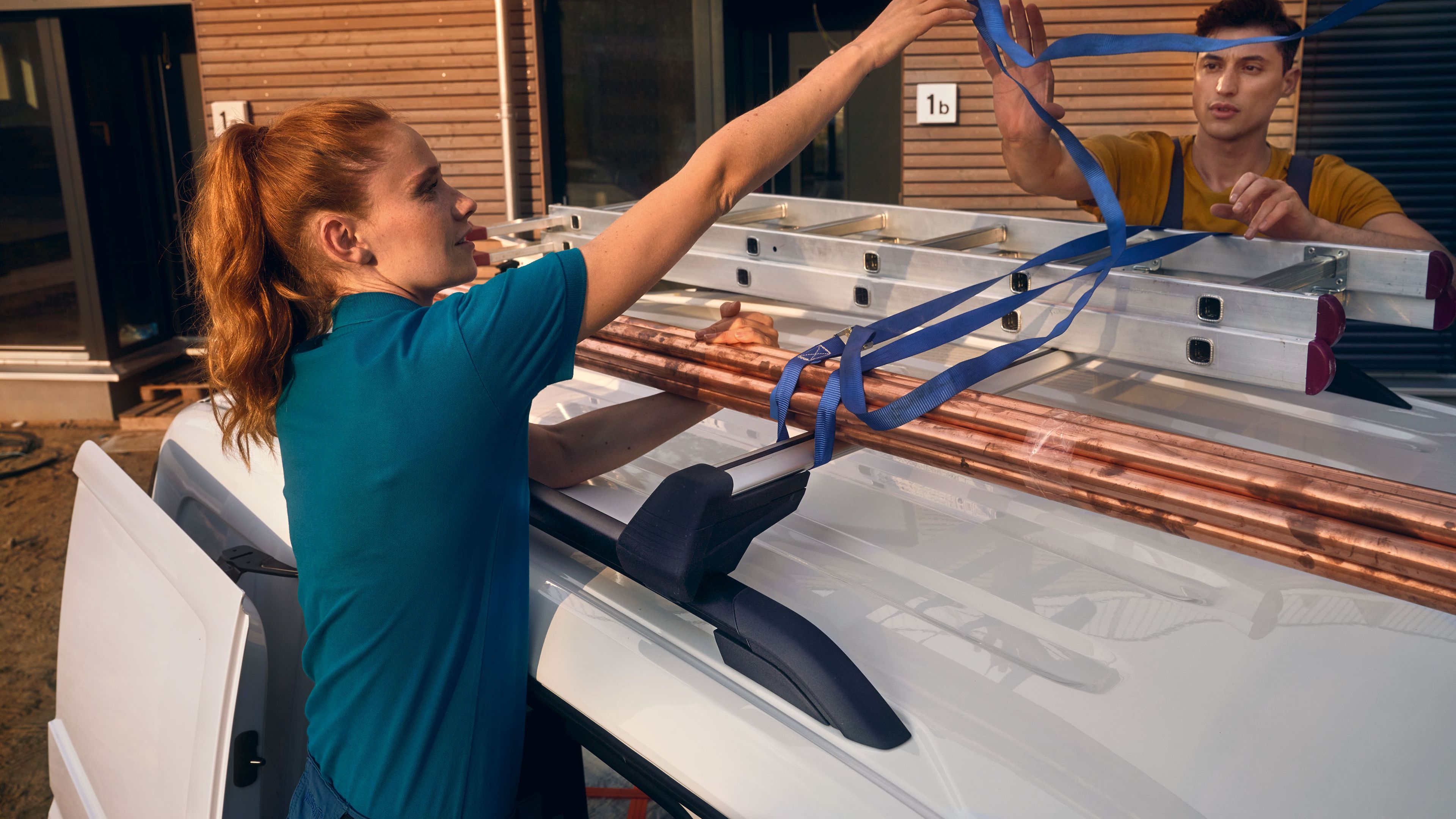 Ein Handwerker-Team fixiert eine Leiter auf der Dachreling eines VW Caddy Cargo.