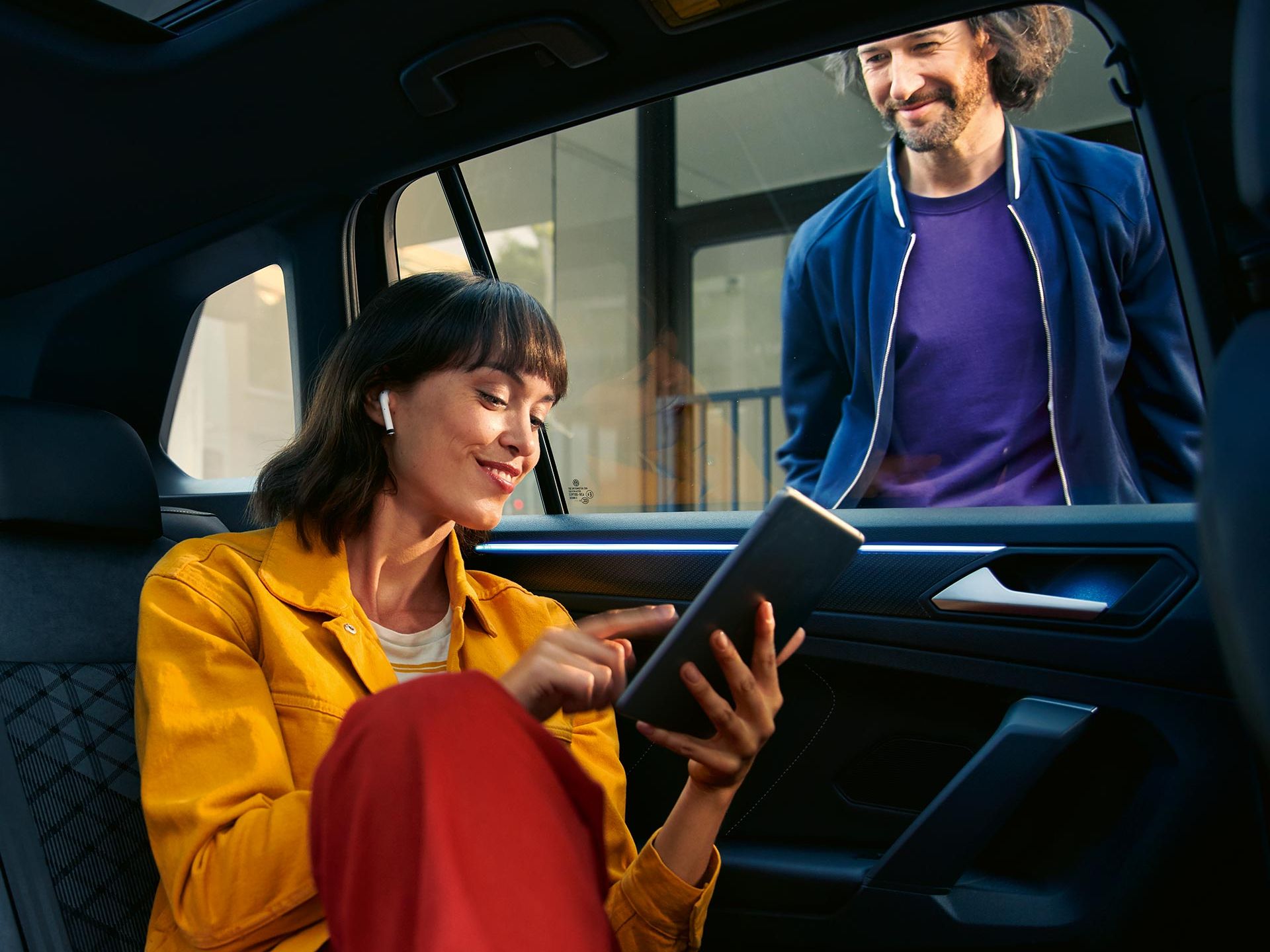 Frau sitzt in VW Tiguan auf Rücksitzbank und verwendet über Tablet We Connect