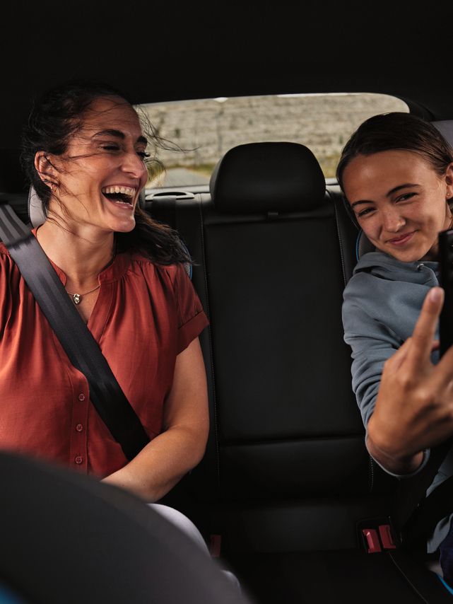 2 Peronen sitzen auf der Rückbank eines Volkswagen und schauen lächelnd auf ein Mobiltelefon