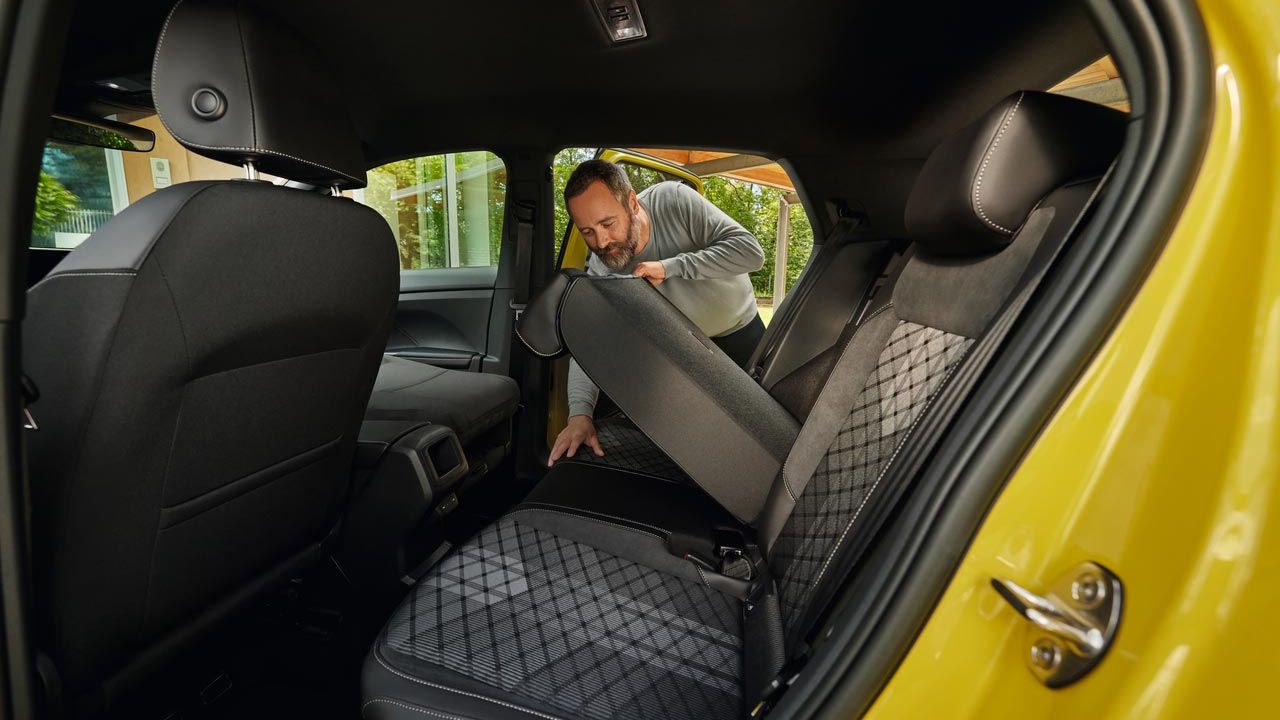 Ein Mann klappt den Rücksitz eines gelben VW T-Cross nach vorne.