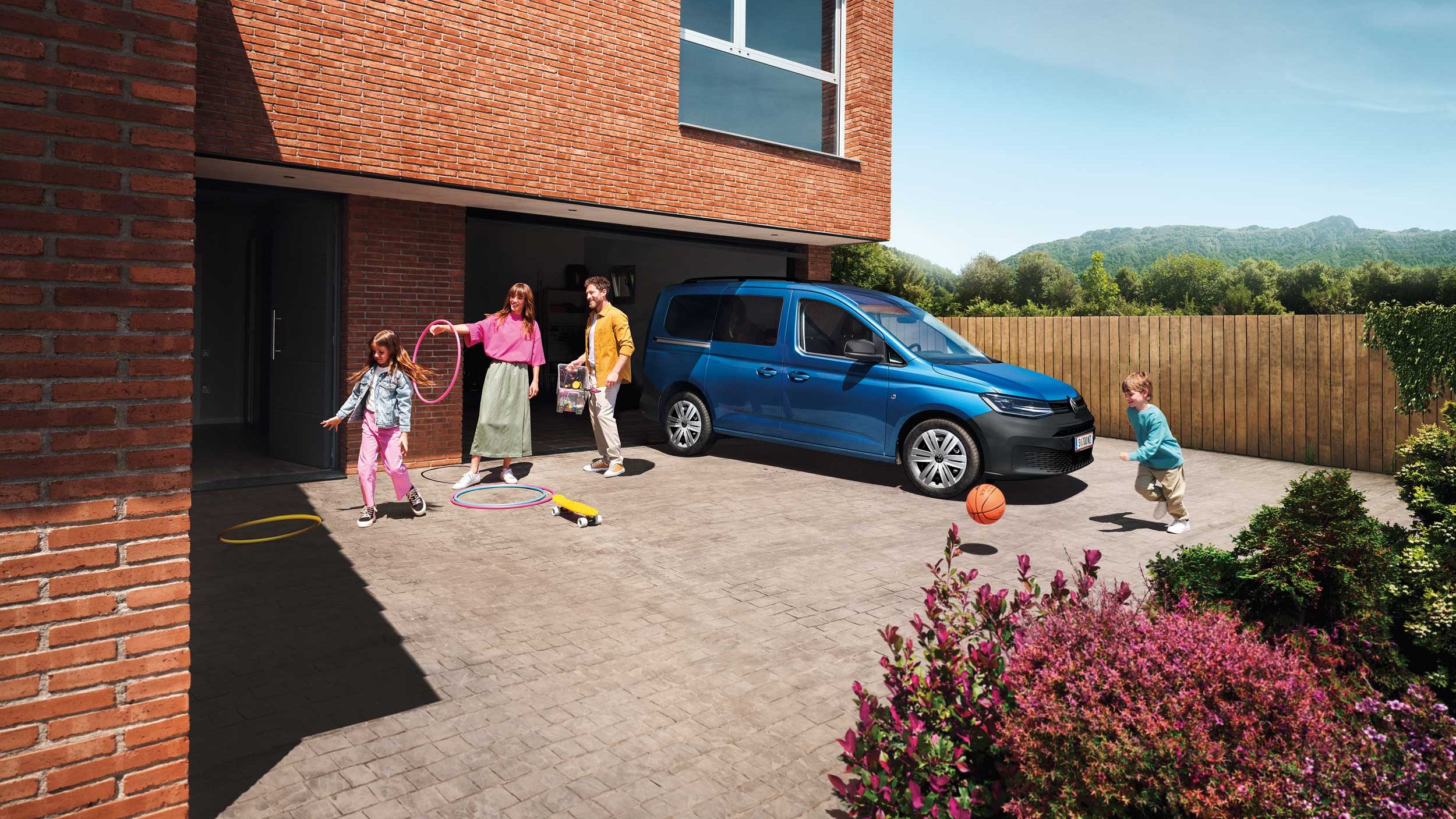 Eine Familie spielt neben einem blauen VW Caddy Family