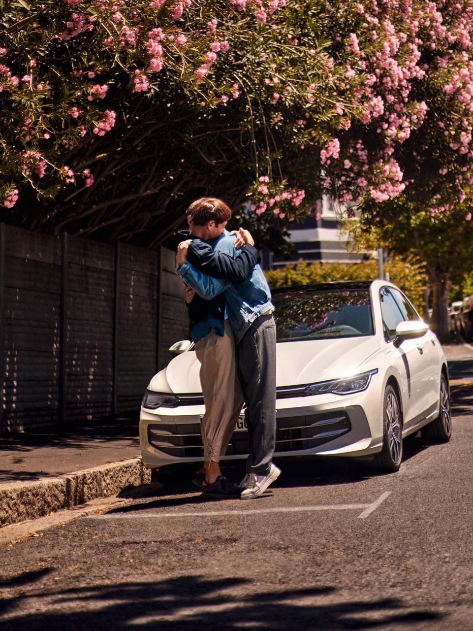 Zwei Männer stehen vor einem weißen VW Golf und umarmen sich