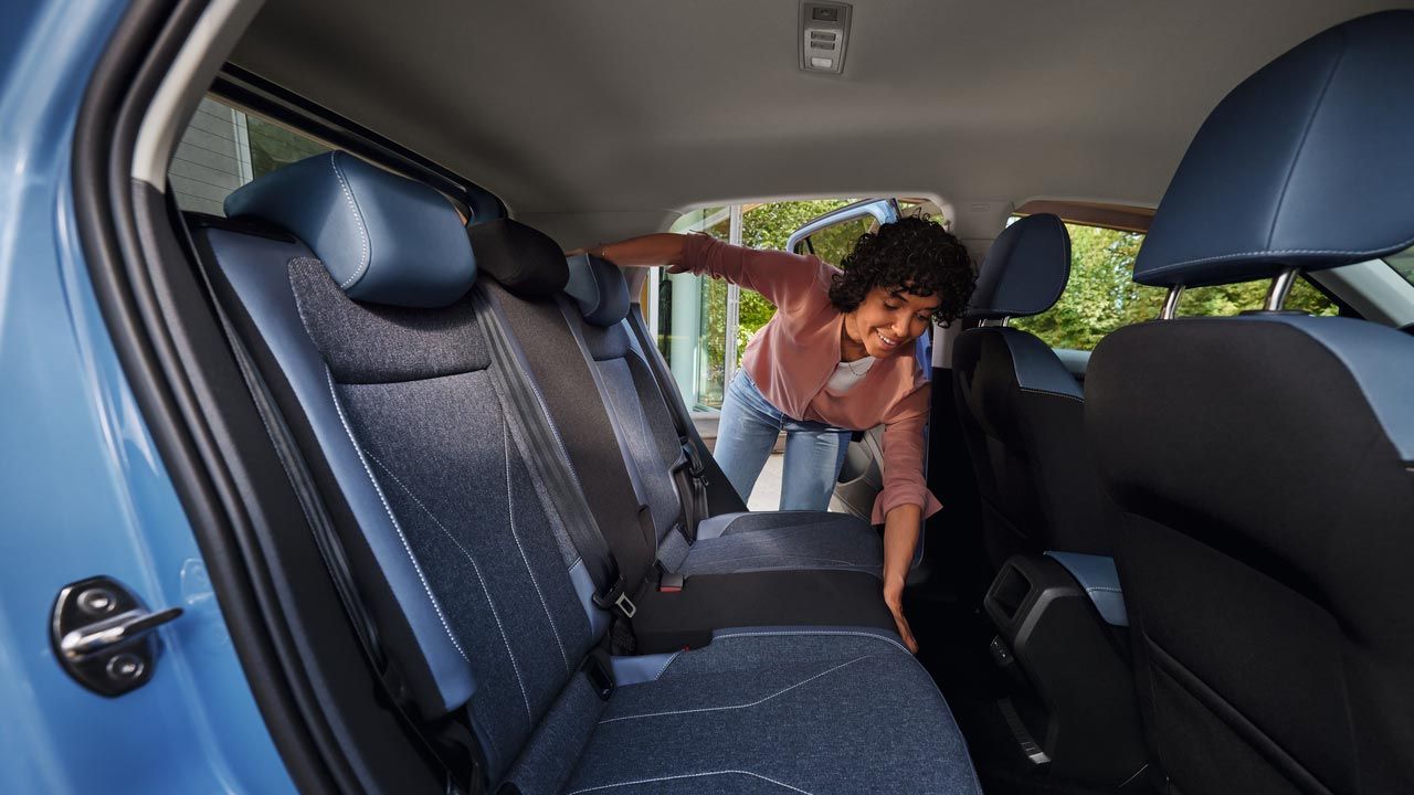 Eine junge Frau ist dabei, den Rücksitz eines blauen VW T-Cross umzuklappen.