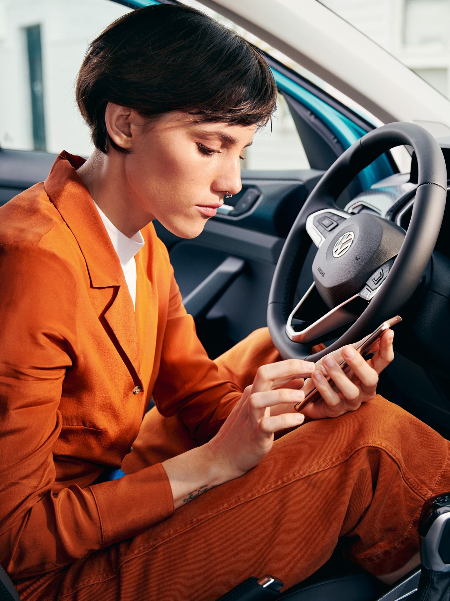 Frau in einem VW T-Cross mit Handy in der Hand und geöffneter Tür.