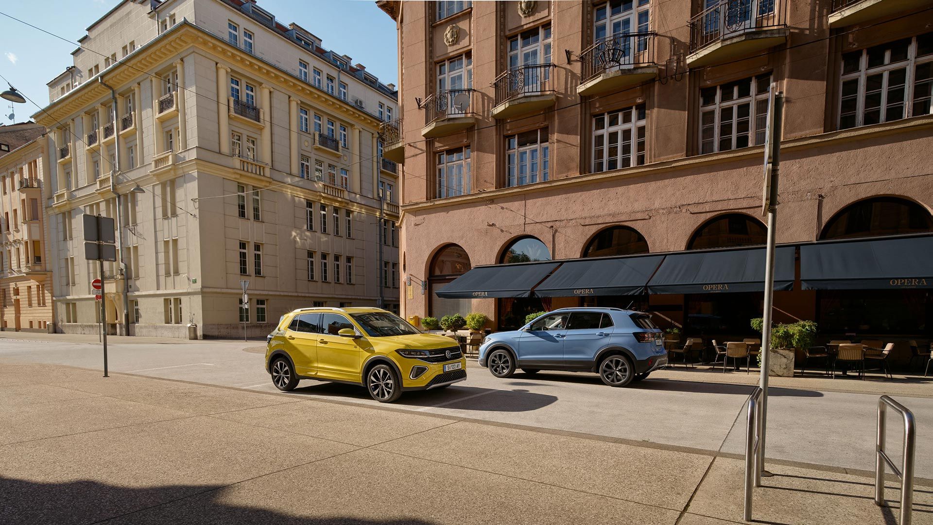 Ein gelber und ein blauer VW T-Cross fahren auf einer Straße aneinander vorbei.