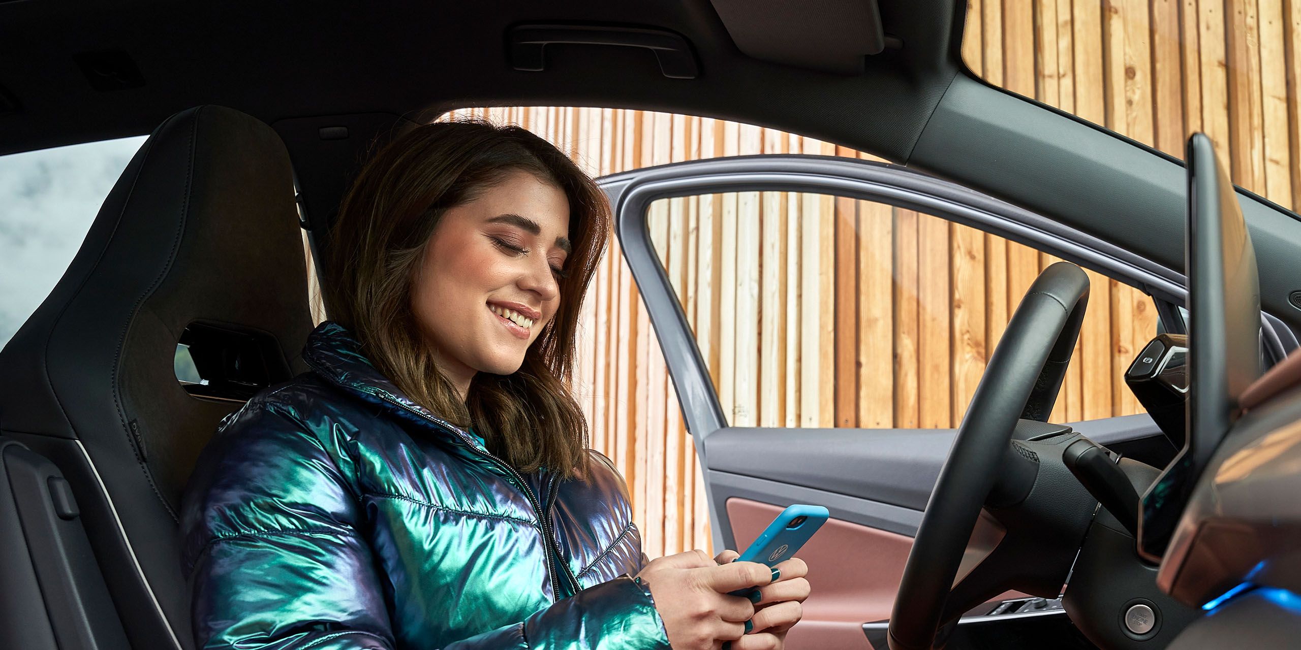 Eine junge Frau sitzt in einem Volkswagen und blickt auf ihr Smartphone
