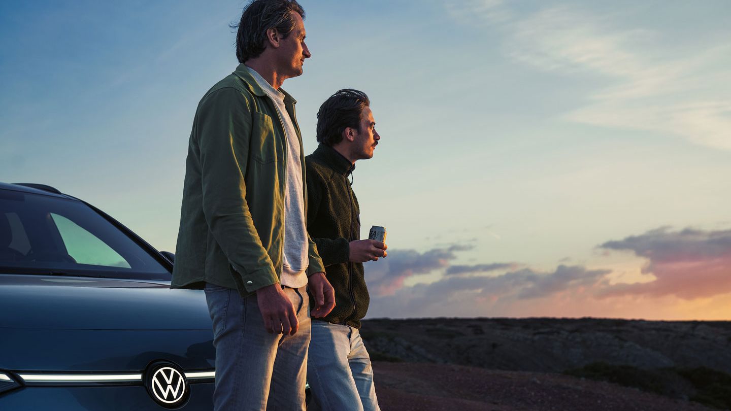 Zwei Männer lehnen an Motorhaube des VW ID.7 Tourer und blicken in die Ferne