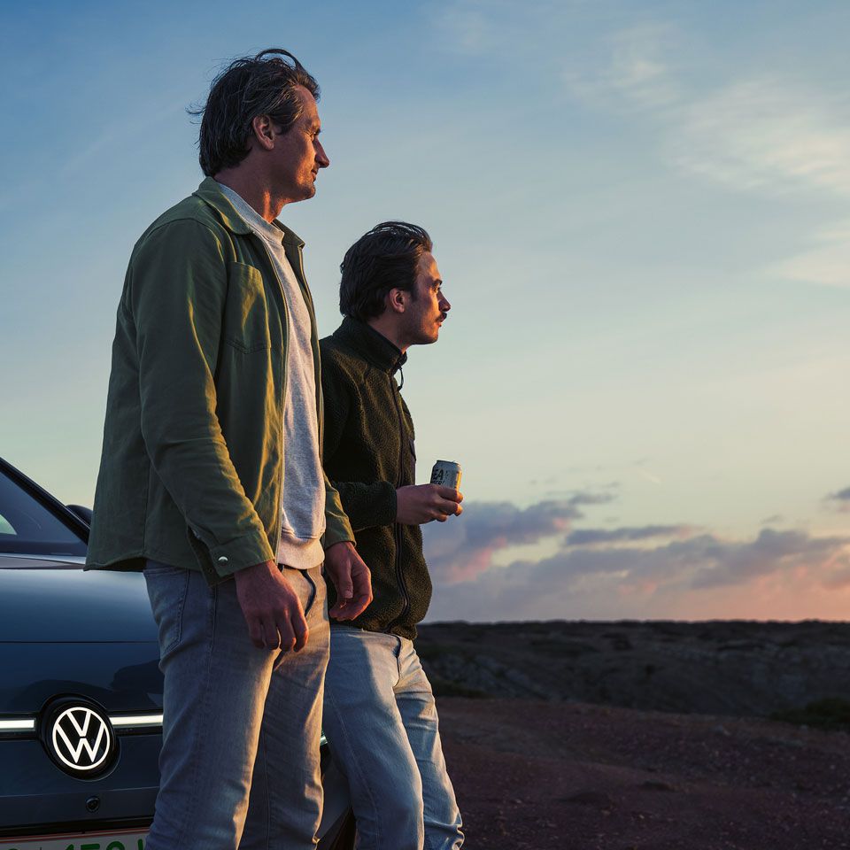 Zwei Männer lehnen an Motorhaube des VW ID.7 Tourer und blicken in die Ferne