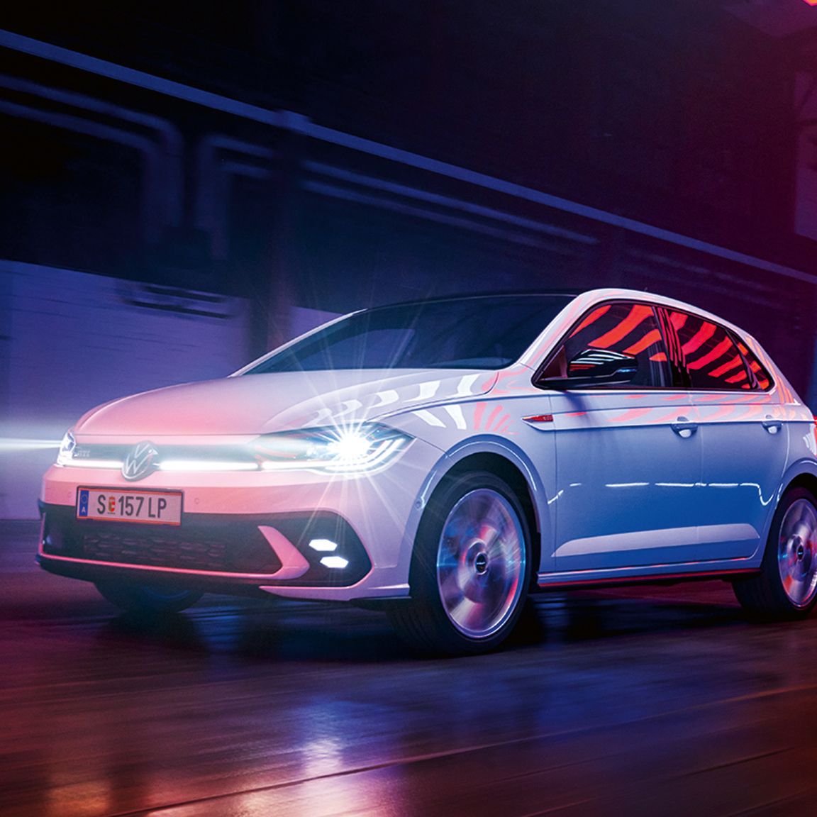 Ein weißer VW Polo GTI fährt in einer Halle mit eingeschalteten LED-Matrix-Scheinwerfern und Lichtleiste in der Front