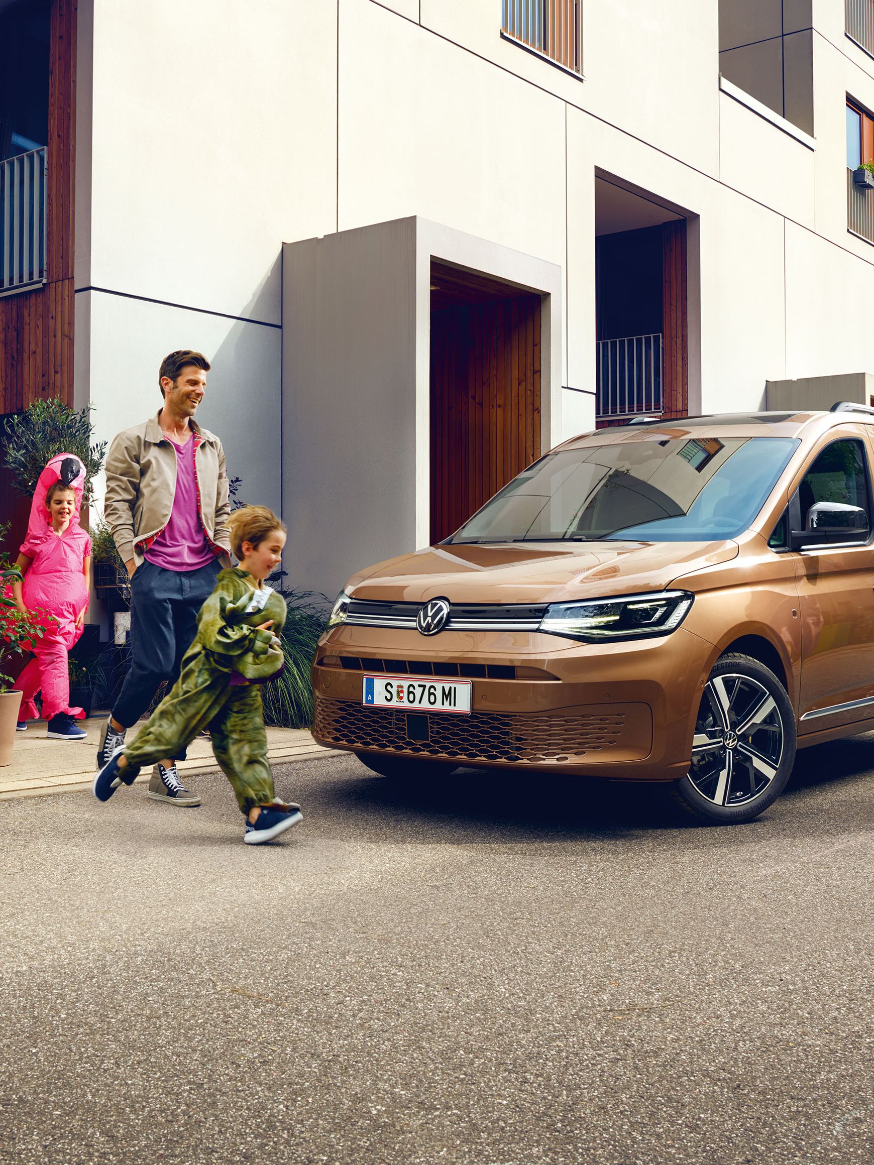 Eine junge Familie steigt vor der Wohnung in einen VW Caddy ein.