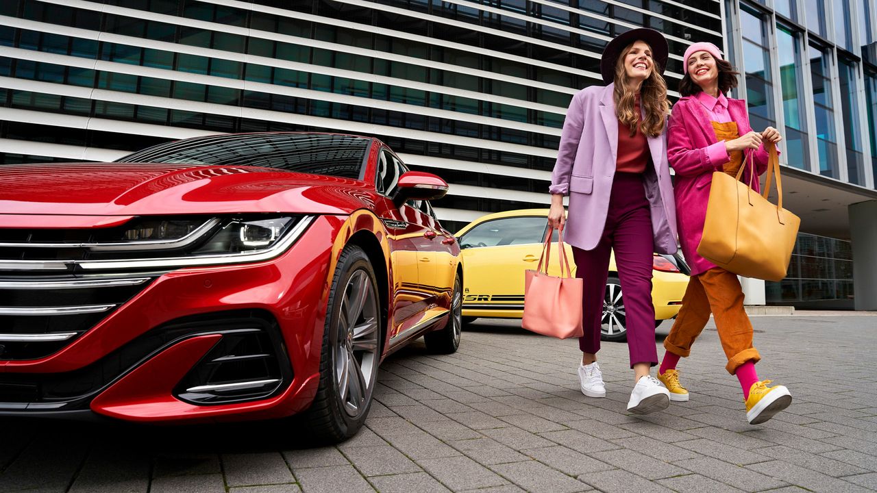 Zwei Frauen entfernen sich im Gespräch und lächelnd von einem Volkswagen