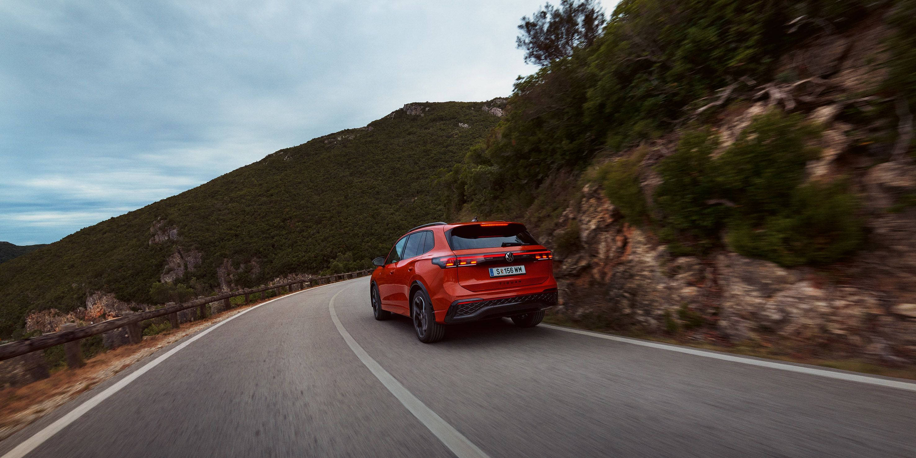 Roter VW Tiguan in Heckansicht fährt durch eine bergige Landschaft.