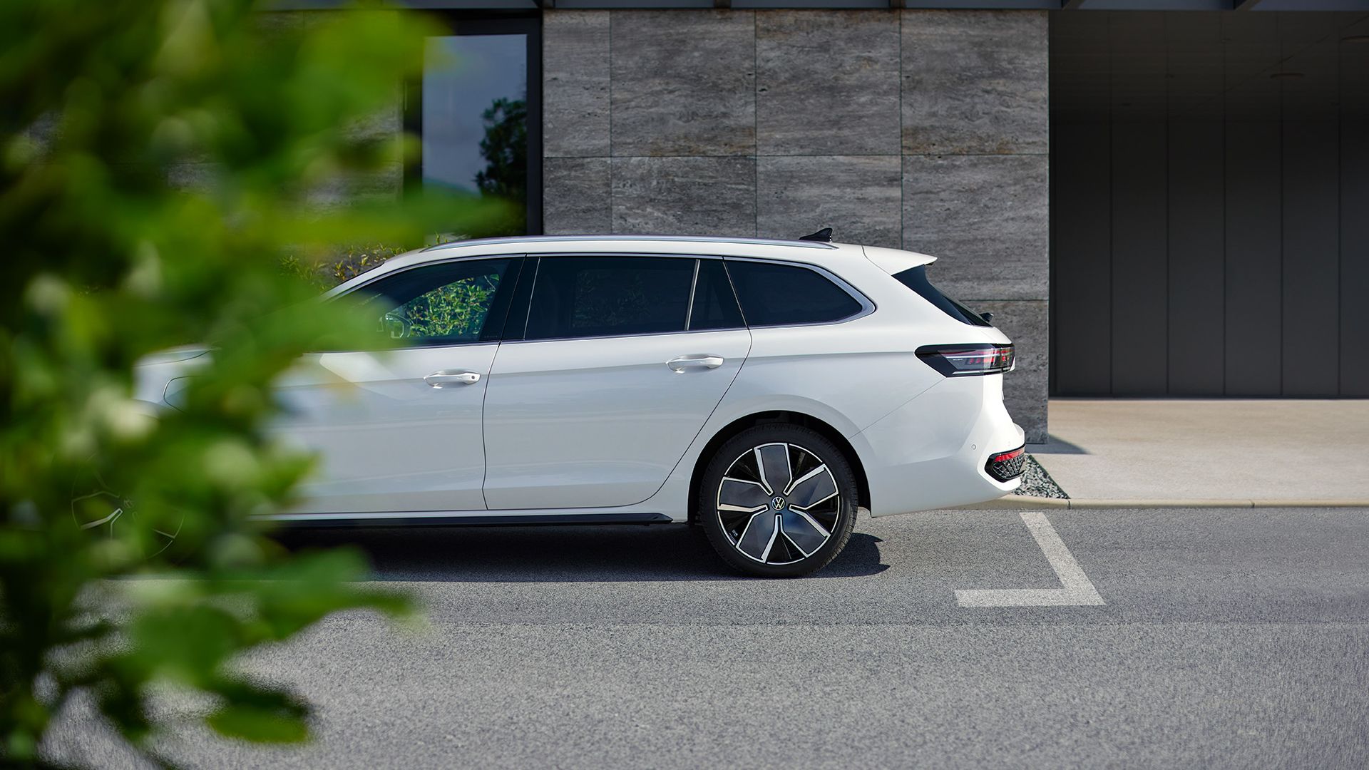 Ein weißer VW Passat steht geparkt vor einem Haus, die Front ist leicht durch einen Busch im Vordergrund verdeckt
