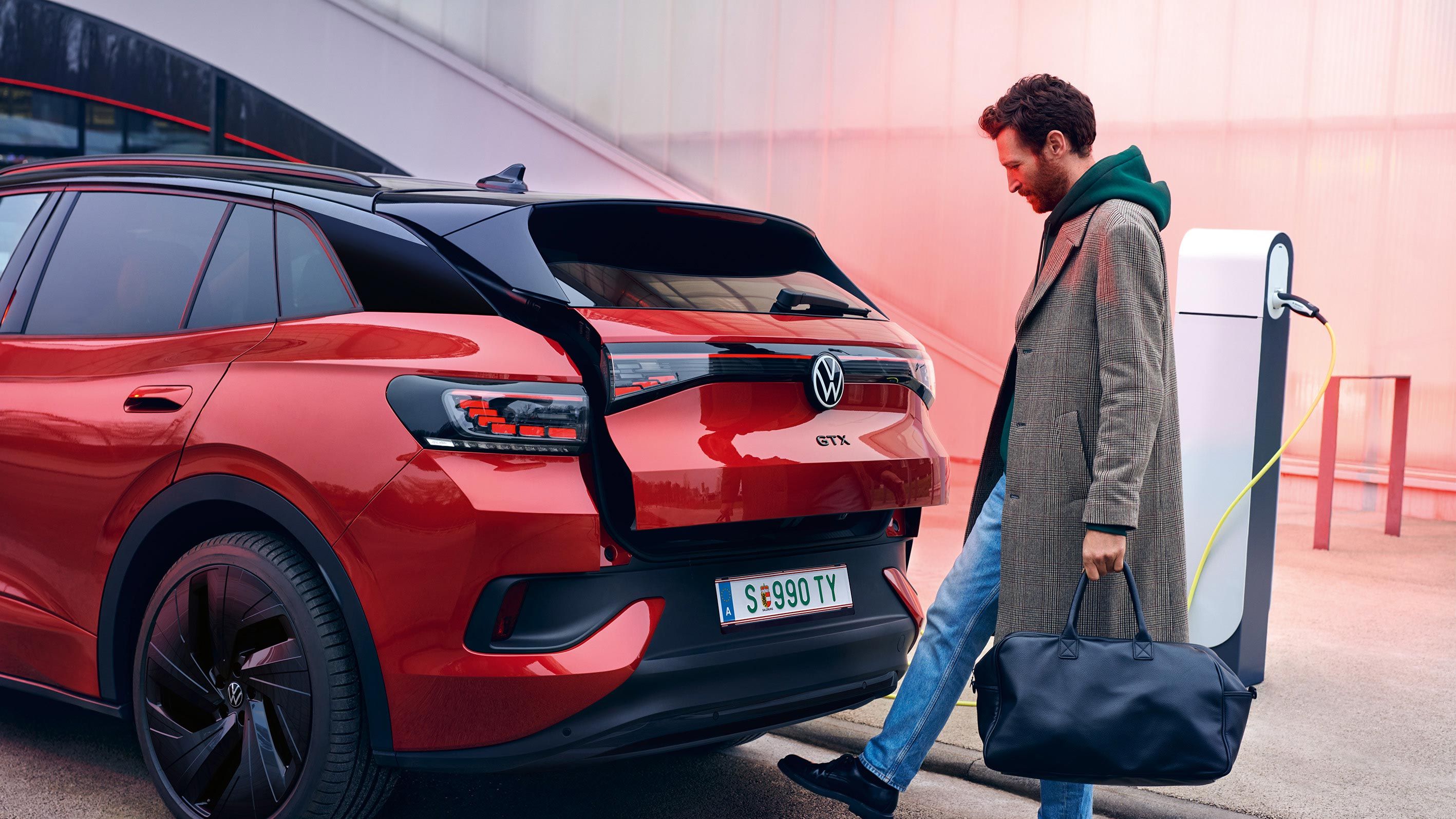VW ID.4 GTX in Rot von hinten zu sehen, Mann mit Tasche öffnet Heckklappe