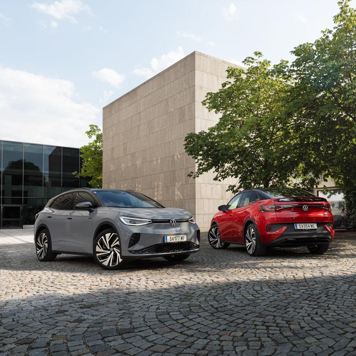 Ein grauer VW ID.4 und ein roter VW ID.5 geparkt vor Gebäude