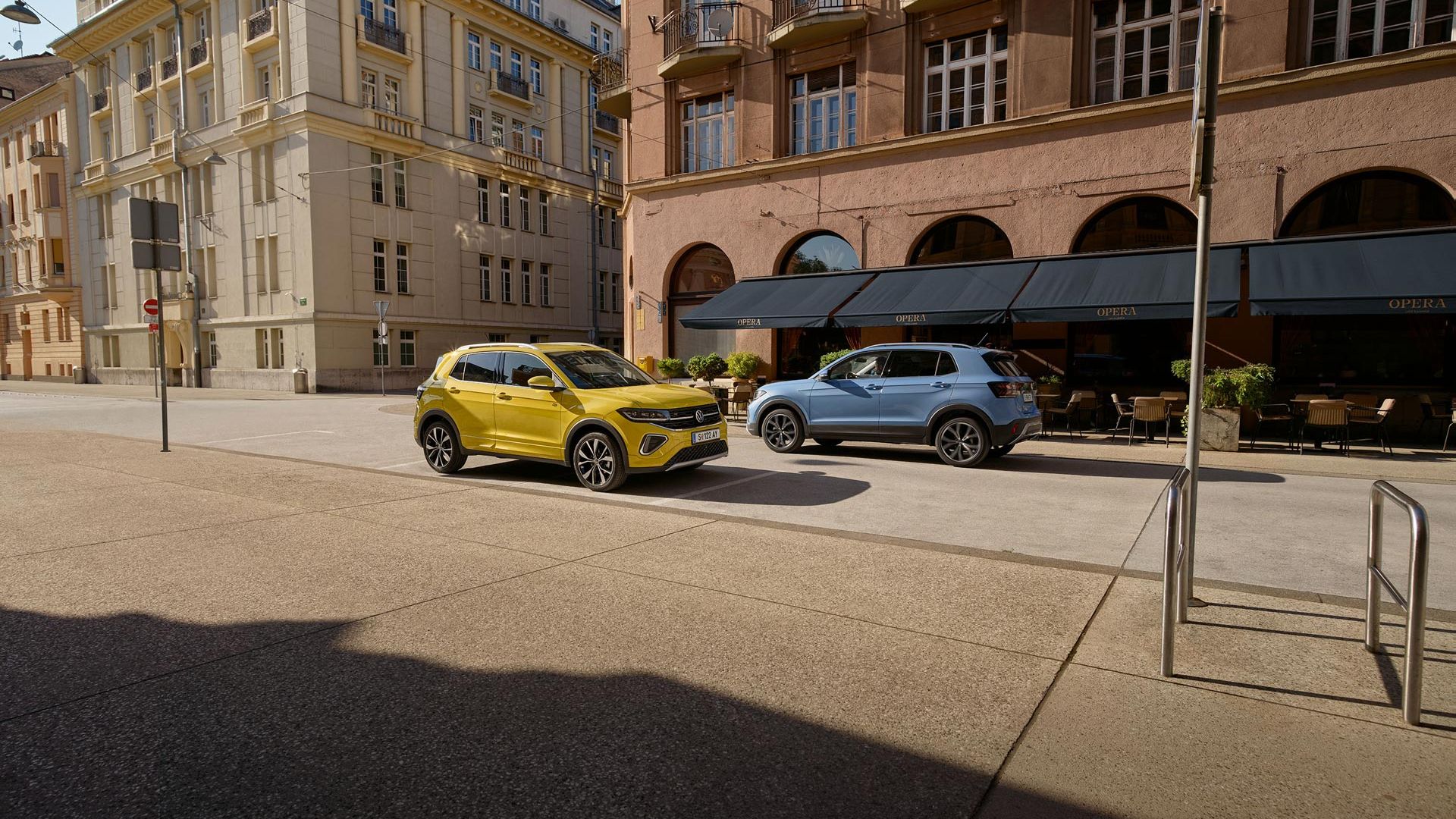 Ein gelber und ein blauer VW T-Cross fahren auf einer Straße aneinander vorbei.